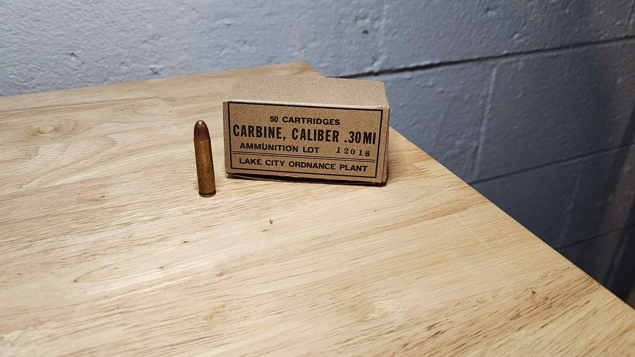 Lake City .30 Carbine cartridge beside a 50-round Lake City Ordnance Plant carton marked lot 12018